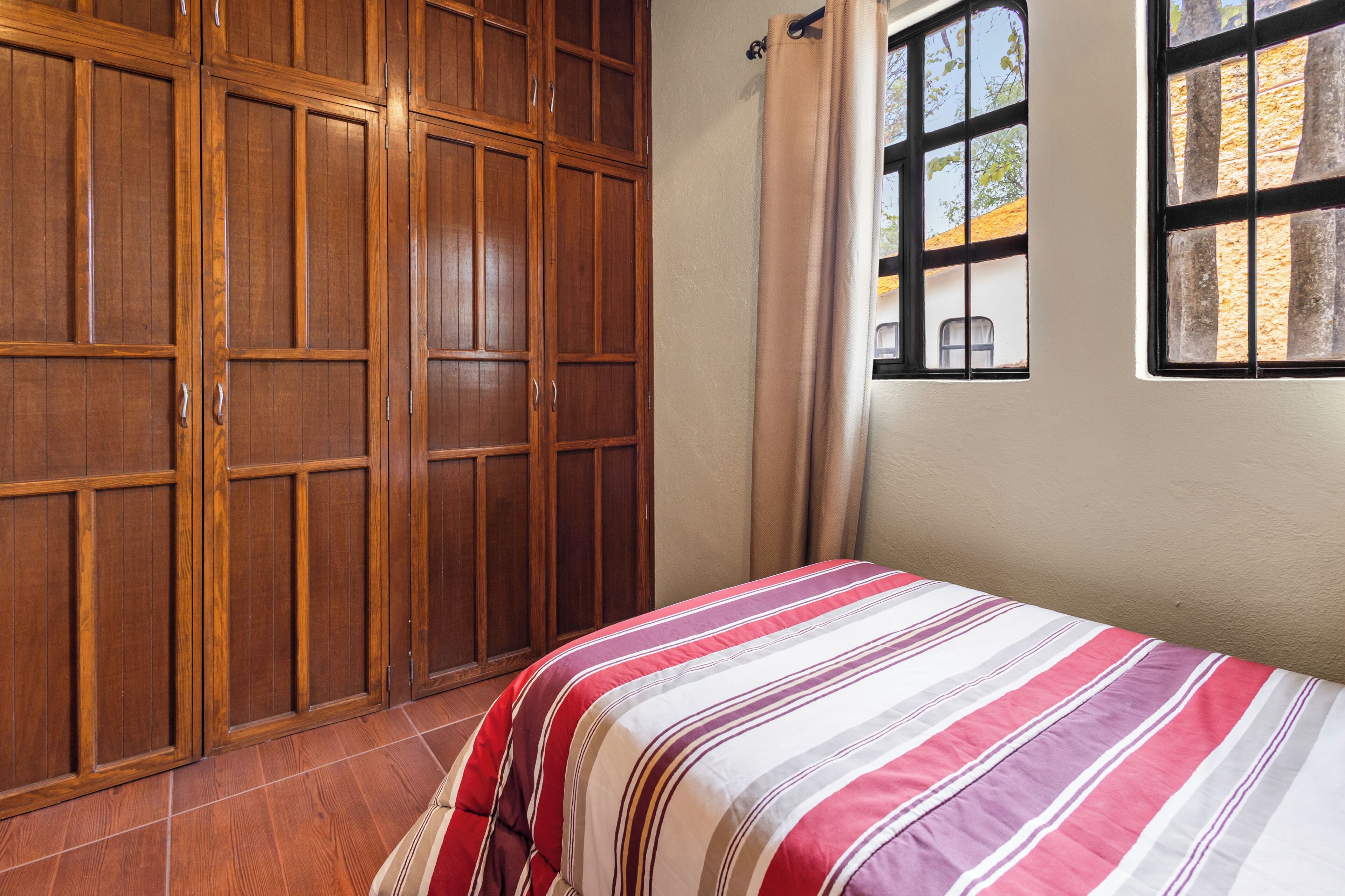 A bedroom with a bed, wooden wardrobe, and a window with curtains.