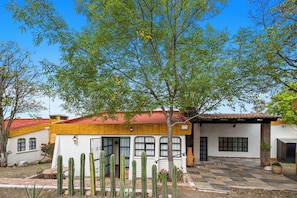 Un edificio tradicional con tejado de tejas rojas, un patio con cactus y un árbol que ofrece sombra.