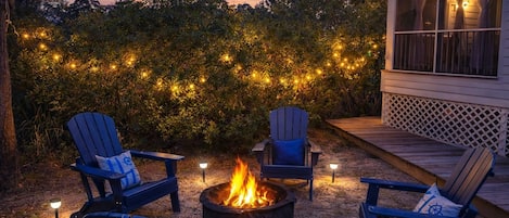 Eine Terrasse mit vier Adirondack-Stühlen, einer Feuerstelle und Lichterketten.