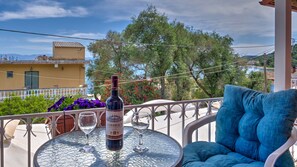 A table with a bottle of wine and two glasses, a blue chair, and a view of a building and trees. - Holiday Home 'Undina Mermaid Sea View' with Wi-Fi and Air Conditioning (Mesongi)