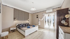 Un dormitorio con cama, mesitas de noche, un armario, una lámpara colgante y vistas a través de un ventanal.