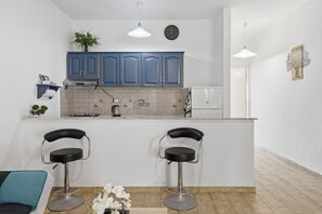 A modern kitchen with two bar stools, a clock, and a plant on the counter. - Undina Mermaid Sea View Country House with Wi-Fi and Air Conditioning (Mesongi)