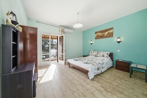 Een slaapkamer met een bed, een kledingkast, een nachtkastje, een bankje en een deur naar een balkon.