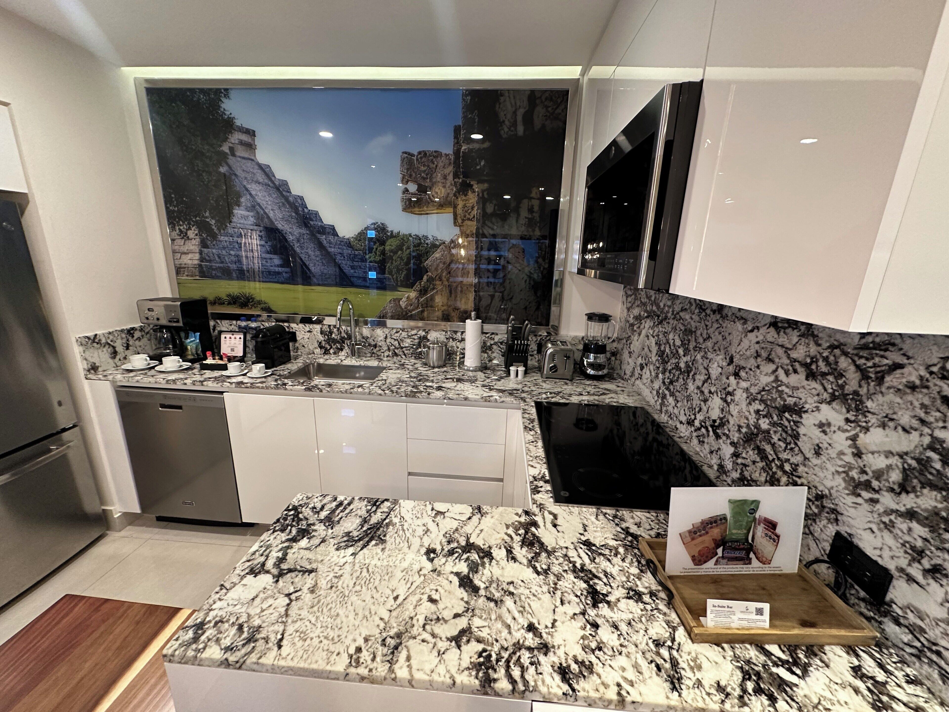 Una cocina moderna con una isla grande, electrodomésticos integrados y un mural de una pirámide.
