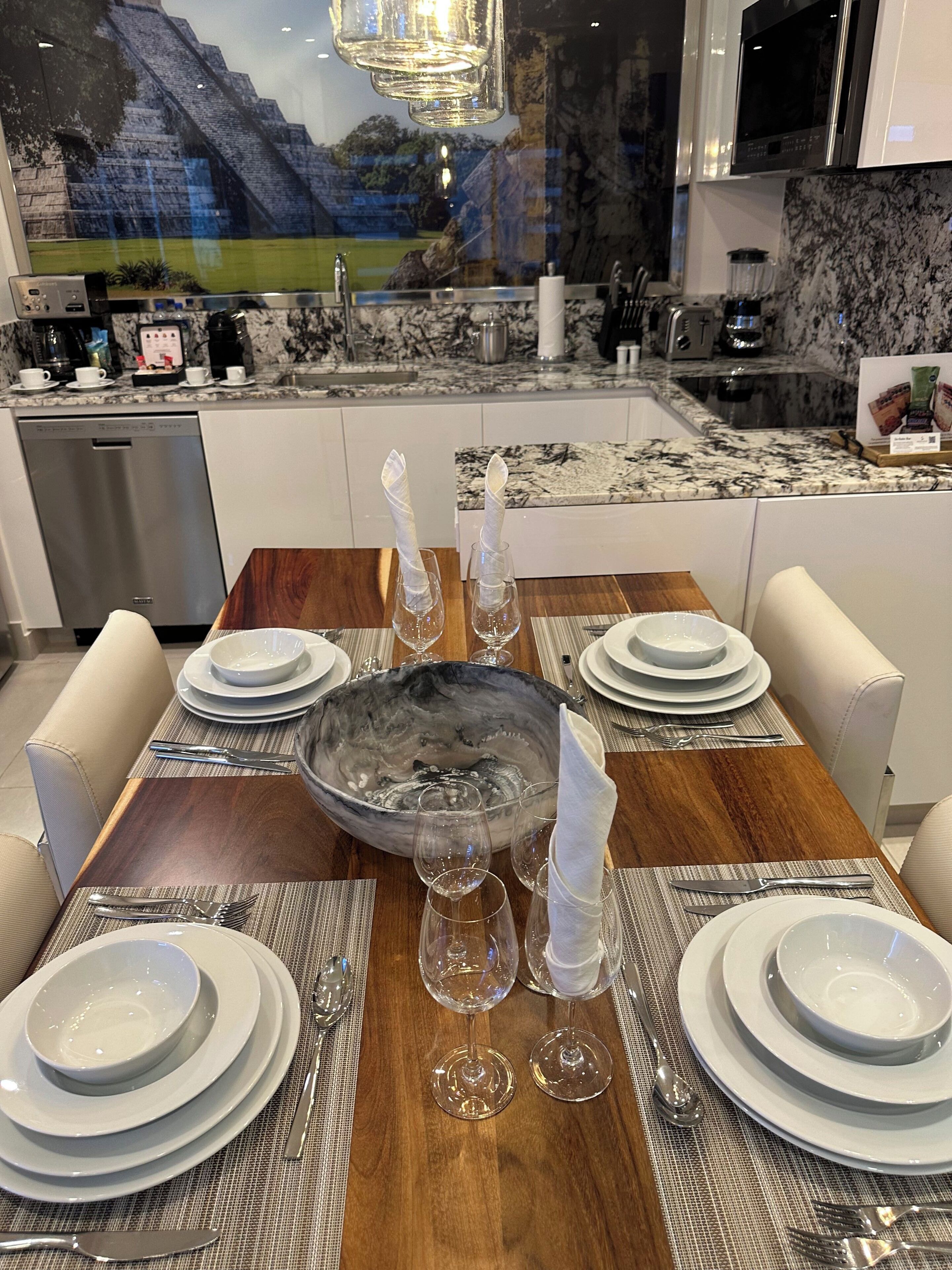 A dining area with a wooden table set for four, surrounded by white chairs.