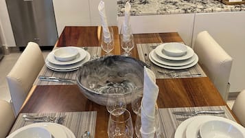 Comedor con mesa de madera dispuesta para cuatro personas, rodeada de sillas blancas.