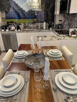 Comedor con mesa de madera dispuesta para cuatro personas, rodeada de sillas blancas.