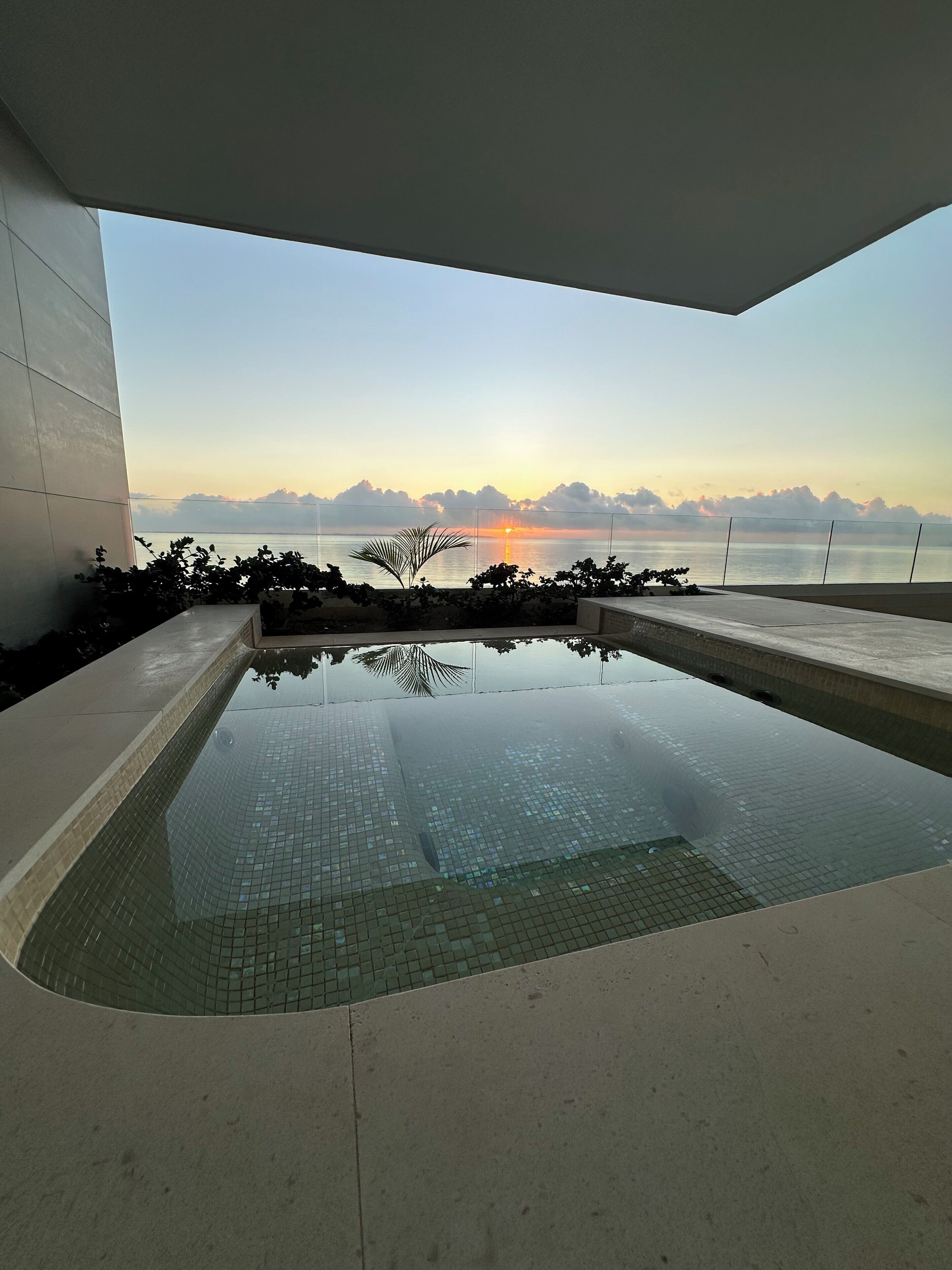 Una piscina moderna con vistas claras al atardecer sobre el agua, rodeada por un muro bajo y algo de vegetación.