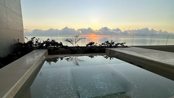 Una piscina moderna con vistas claras al atardecer sobre el agua, rodeada por un muro bajo y algo de vegetación.