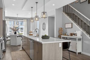 Una cocina moderna con una isla central, iluminación colgante y una escalera.