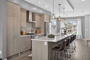 A modern kitchen with wooden cabinets, a central island with bar stools, stainless steel appliances, and pendant lighting. - Calgary Urban Lodge: Hot Tub, Sauna, Game Room (Calgary)