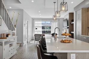 A modern kitchen with a central island, pendant lighting, and a view to the dining area. - Calgary Urban Lodge: Hot Tub, Sauna, Game Room (Calgary)