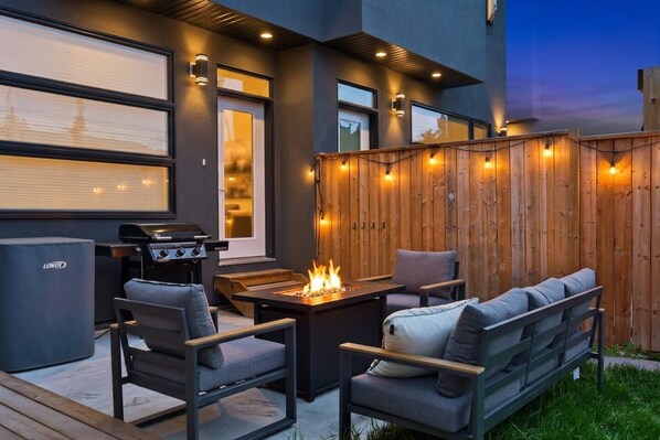 Un patio exterior con una parrilla, asientos y un pozo de fuego.
