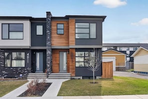 A modern two-story residential building with a prominent stone facade, large windows, and a small front yard.