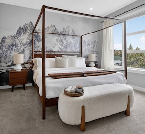 A four-poster bed with a mountain mural, a bedside table with a lamp, and a view of the outdoors.