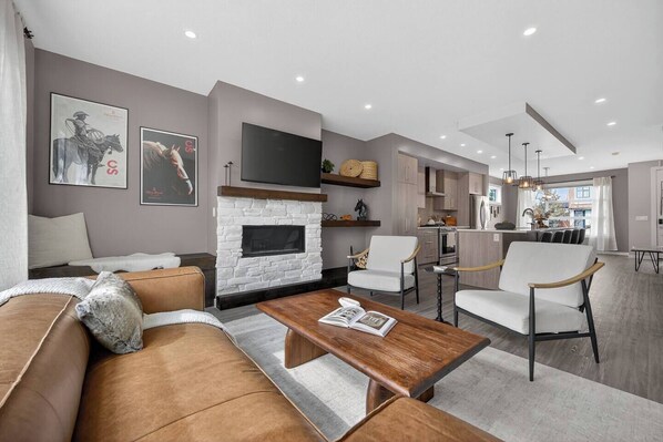 A modern living room with a fireplace, a sofa, a coffee table, and a dining area with chairs.