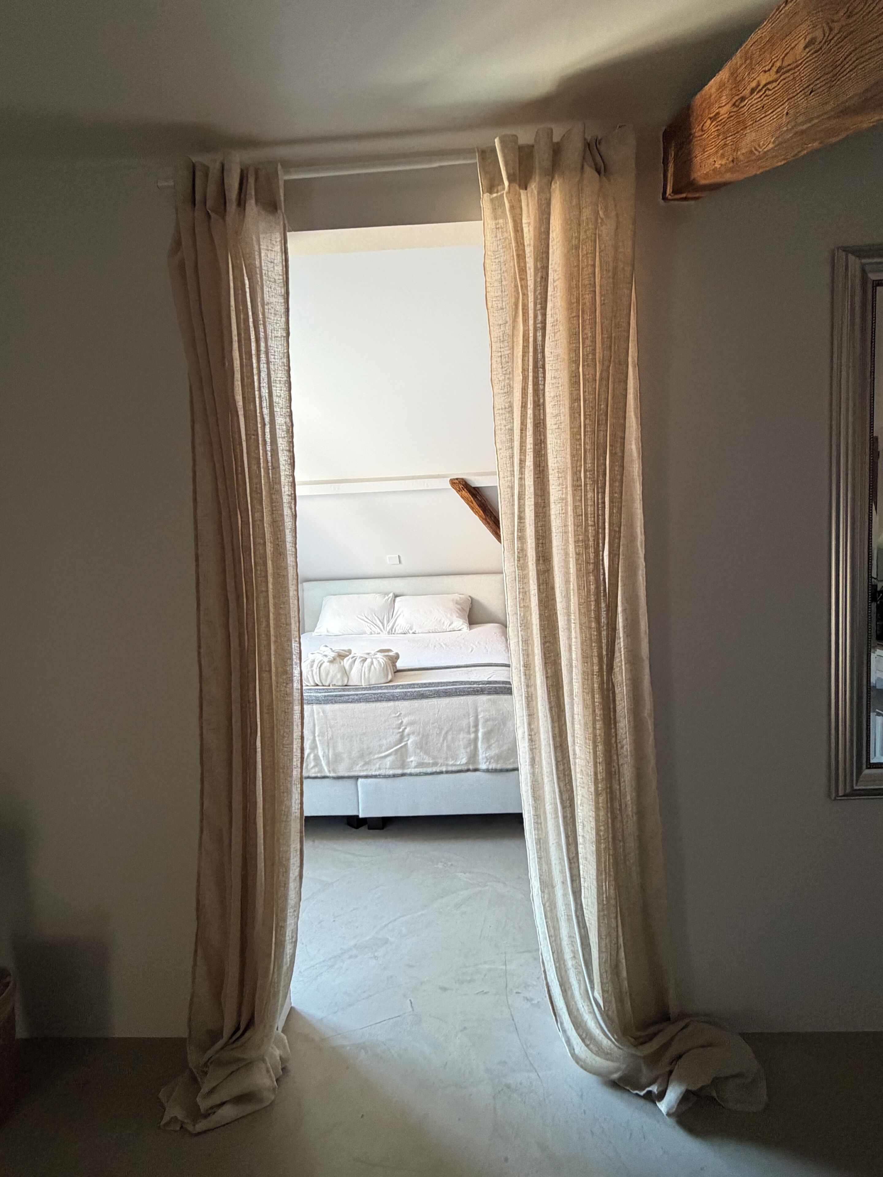 A bedroom with a bed, curtains, and a wooden beam on the ceiling.