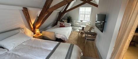 A bedroom with two beds, a small table, a chair, and a window.