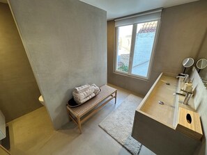 A bathroom with a wooden bench, a sink with a mirror, and a window with a view of a building. - Your home in Bruges, set in a historic setting just 5 minutes from the Main Market Square. (Brugge)