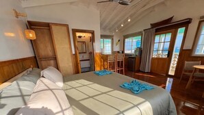 Ein geräumiges Schlafzimmer mit einem großen Bett, Holzboden und Meerblick durch die Fenster.