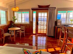 A room with wooden flooring, a dining table with chairs, a small kitchen area, and large windows with a view of the sea. - Ocean View Bungalow (#2) (Bocas del Toro)