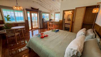 A spacious room with a large bed, a dining area, and a view of the ocean.