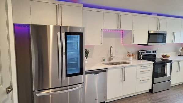 Una cocina moderna con electrodomésticos de acero inoxidable, armarios blancos e iluminación LED debajo de los gabinetes.