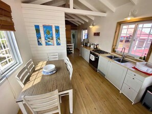 Eine Küche mit Essbereich, Holzboden, weißen Schränken und einem Fenster mit Jalousien.
