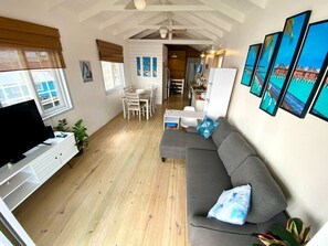 Ein großzügiger Wohnbereich mit grauem Sofa, einem Flachbildfernseher, Holzböden und einem Essbereich mit weißer Möbel.