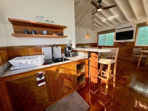 A kitchen with wooden cabinets, a built-in stove, a sink, and a dining area with a table and chairs. - Water Front Bungalow (#1) (Bocas del Toro)
