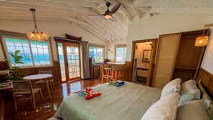 A spacious room with a large bed, a dining area, and a view of the ocean. - Water Front Bungalow (#1) (Bocas del Toro)