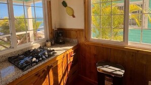 A kitchen with wooden cabinets, a gas stove, a coffee maker, and a trash can. - Water Front Bungalow (#1) (Bocas del Toro)