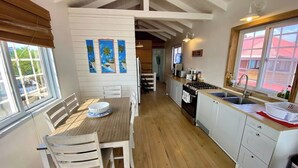 Eine Küche mit Holzboden, weißen Schränken, einem Essbereich mit Tisch und Stühlen sowie Bildern an der Wand.