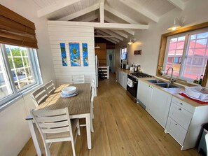 Eine Küche mit Holzboden, weißen Schränken, einem Essbereich mit Tisch und Stühlen sowie Bildern an der Wand.