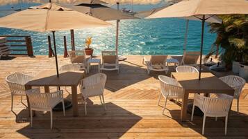 A wooden deck with tables and chairs, umbrellas, and a view of the ocean.