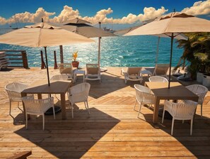 Eine Holzterrasse mit Tischen, Stühlen und Sonnenschirmen, mit Blick auf das Meer.