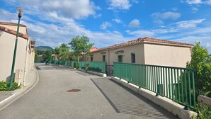 A street with buildings, green fences, and a clear sky. - A terrace and sunshine just outside Nice (Saint-Blaise)