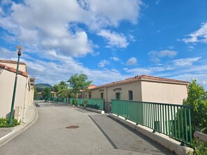 A street with buildings, green fences, and a clear sky. - A terrace and sunshine just outside Nice (Saint-Blaise)