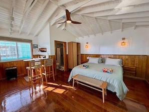 Une chambre spacieuse avec un grand lit, un banc en bois, un bureau et un ventilateur de plafond.