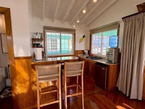Une cuisine avec des meubles en bois, un coin bar avec deux chaises en osier, une machine à café, un grille-pain et un distributeur d’eau.
