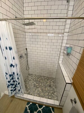 Une douche avec des murs recouverts de carreaux blancs et un pommeau de douche.