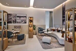 A modern living room with a sofa, chairs, a coffee table, and a bookshelf. - Marriott Dubai | Deluxe | Sheikh Zayed Road Base for Work and Long Stays (Dubai)