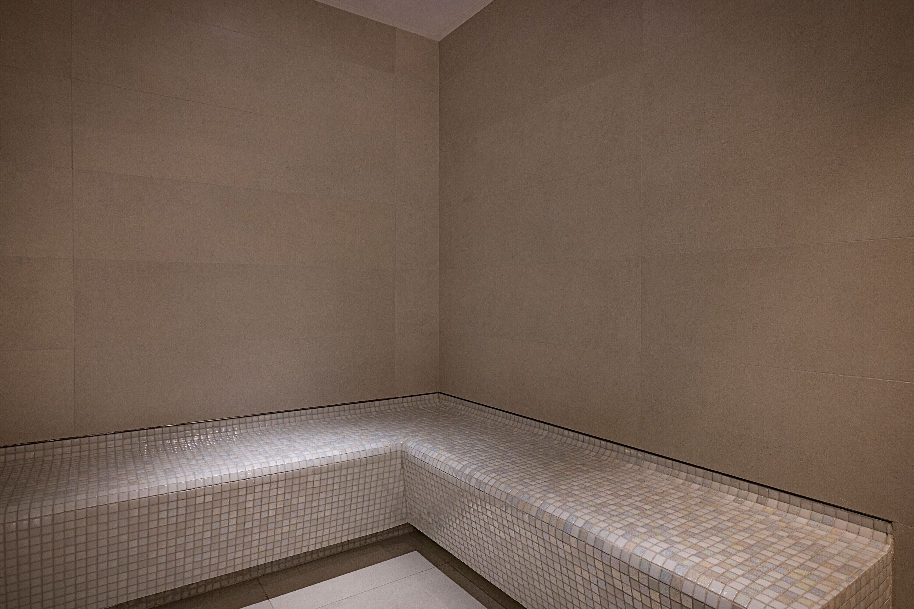 A corner of a room with tiled walls and a bench.