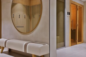 A restroom with a bench, a round mirror, and wooden lockers. - Marriott Dubai | Deluxe | Sheikh Zayed Road Base for Work and Long Stays (Dubai)