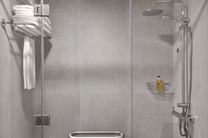 Una doccia con soffione a mano, un portascopini con asciugamani piegati e un dispenser di sapone su uno scaffale.