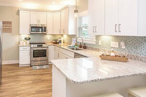 Una cocina moderna con armarios blancos, electrodomésticos de acero inoxidable, encimera de granito y salpicadero con azulejos pequeños.
