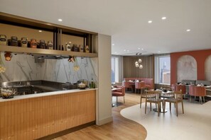 Una cucina moderna con un piano di lavoro in legno, un'area pranzo con sedie e tavoli, e vista sulla città attraverso ampie finestre.
