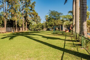 Un espacio al aire libre con césped, árboles, una cerca y una estructura que parece ser una zona de juegos o una cancha deportiva.
