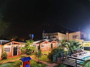 Un hotel con varias habitaciones, piscina y un depósito de agua al fondo.