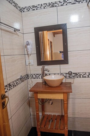 Un baño con un mueble de tocador de madera, un lavabo blanco, un espejo y una pared de azulejos con diseño de cuadros.